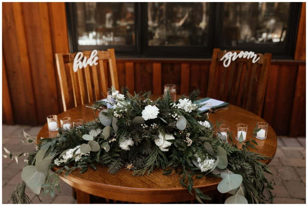 wedding sweetheart table with bride and groom signs and flowers decorating the table.