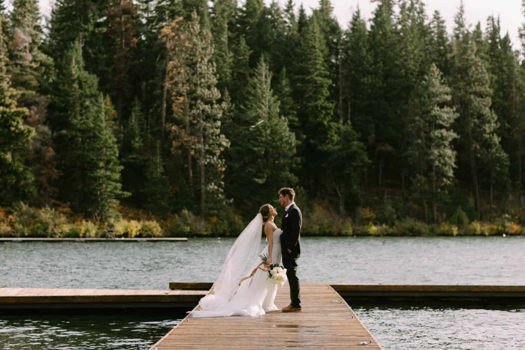 couple dressed in wedding attire standing on a dock and looking at each other.