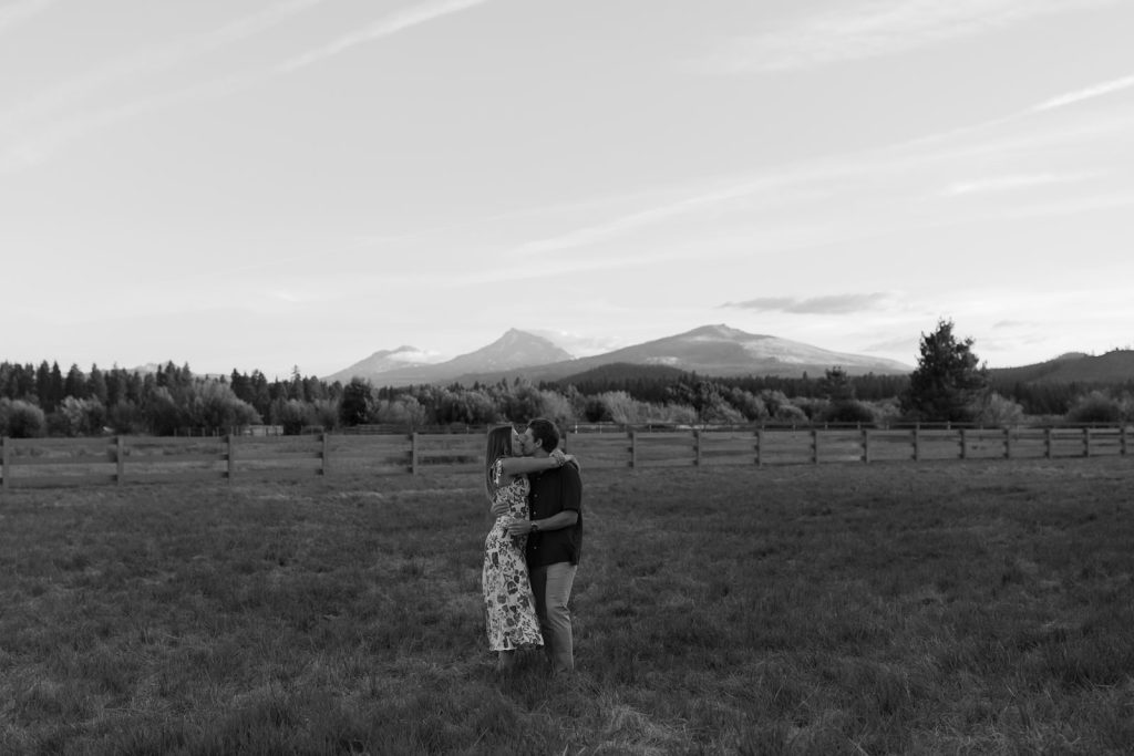 a couple embracing in a kiss at black butte ranch in the middle of a field, with the cascade mountains behind them.
