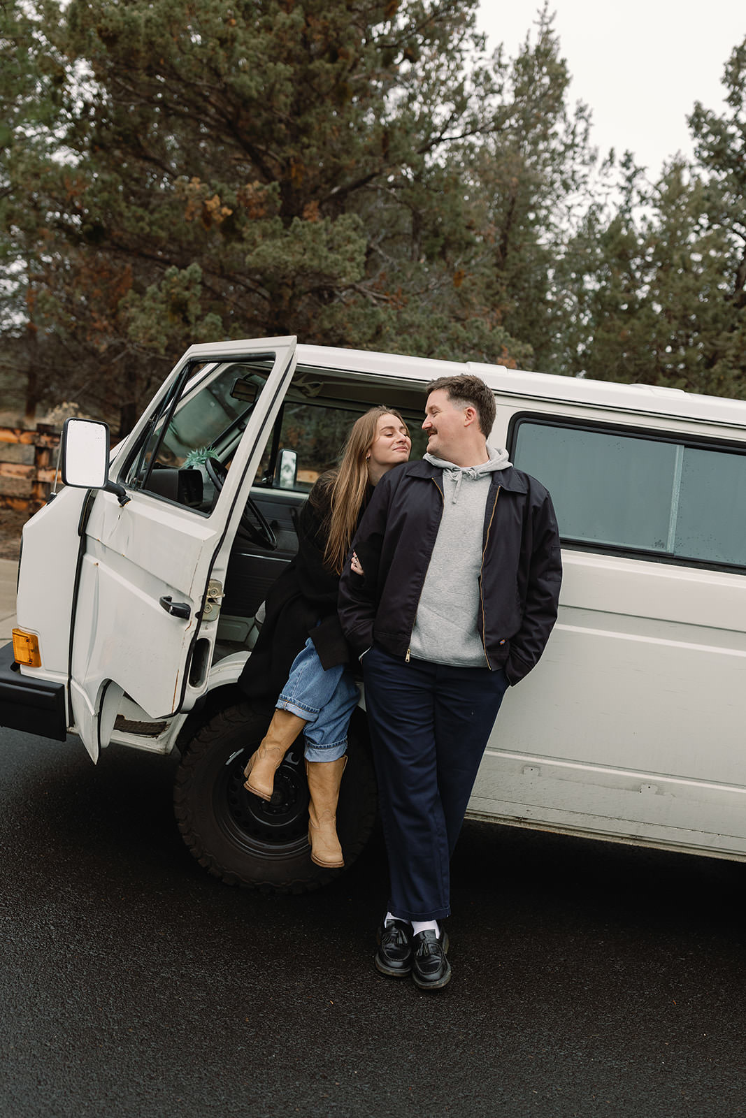 engaged couple standing by their white van and smiling at each other for a photo